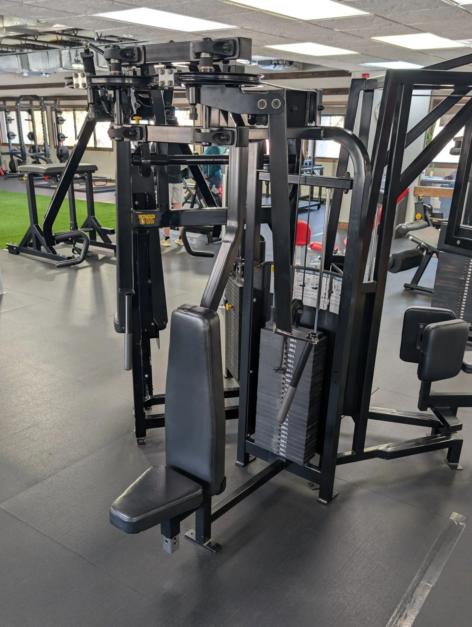 A multi-functional gym machine in a fitness center with various adjustable parts and weight stacks.