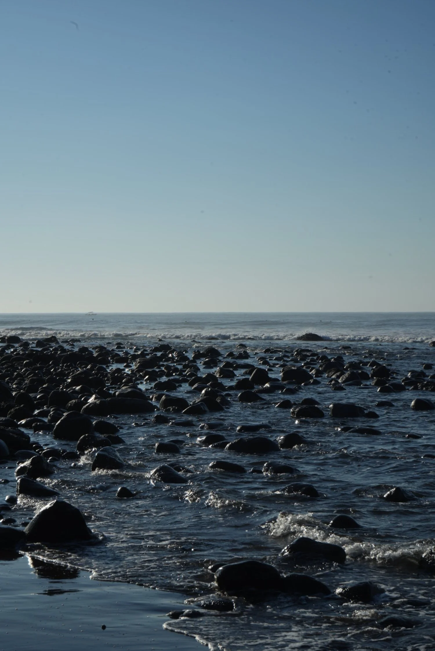 A rocky beach with water and a clear blue sky in the background.