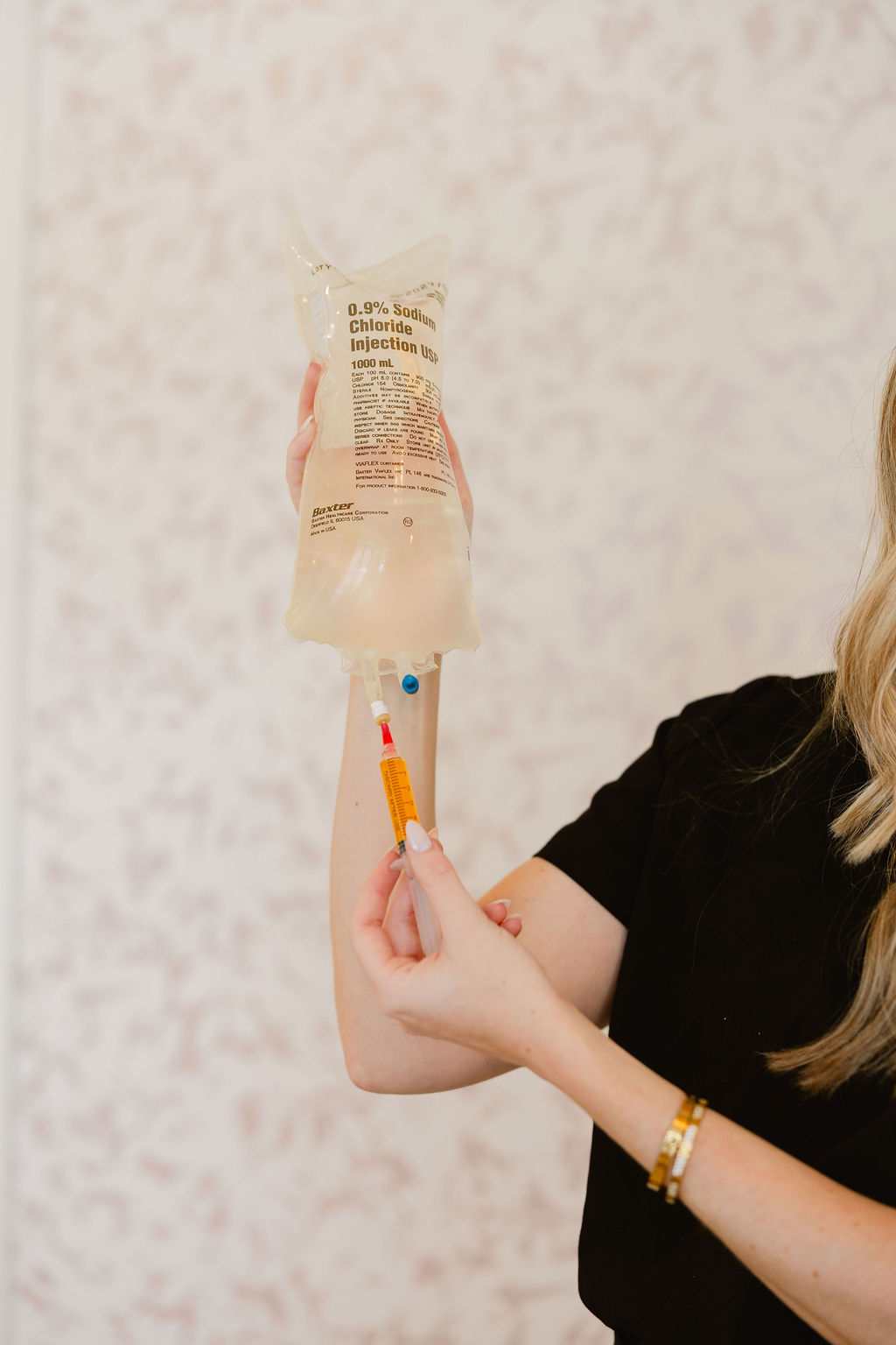 A person holding an IV bag labeled '0.9% Sodium Chloride Injection USP 1000 mL' and drawing liquid with a syringe.