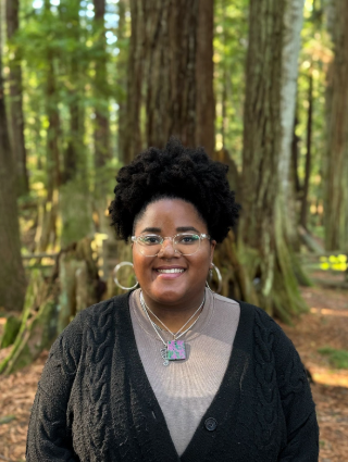 woman with glasses and curly hair smiling in a forest setting