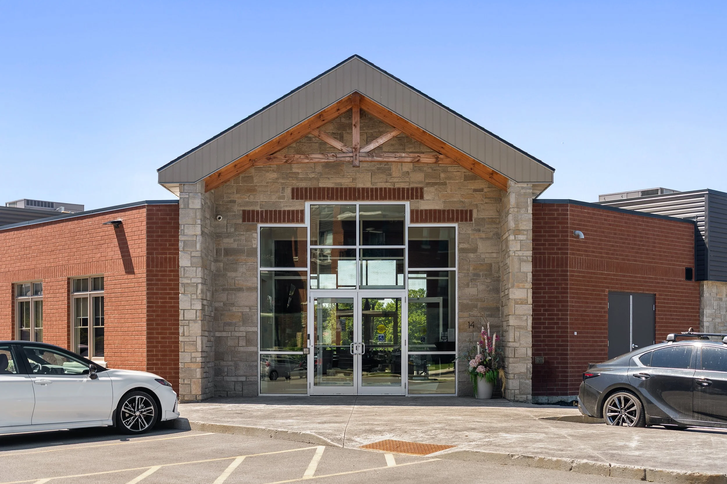 Front entrance of a modern stone and brick building featuring a grand gabled glass doorway set under a clear blue sky.