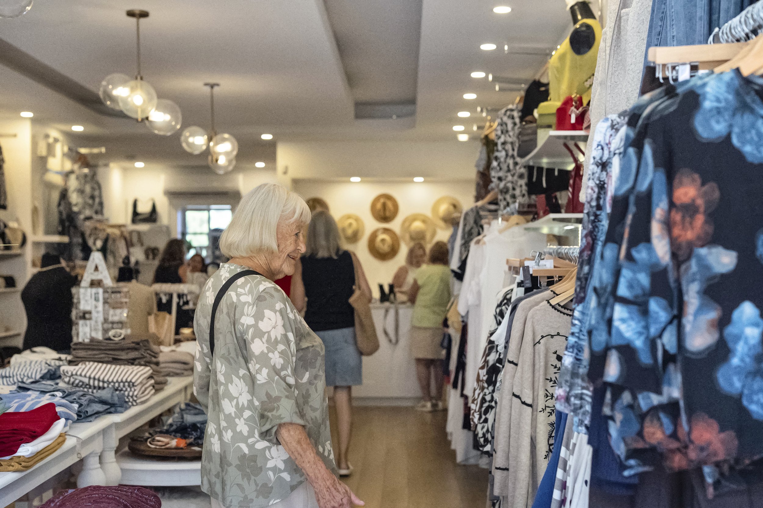 An older woman browsing through clothing hanging on racks inside a bright, modern boutique shop
