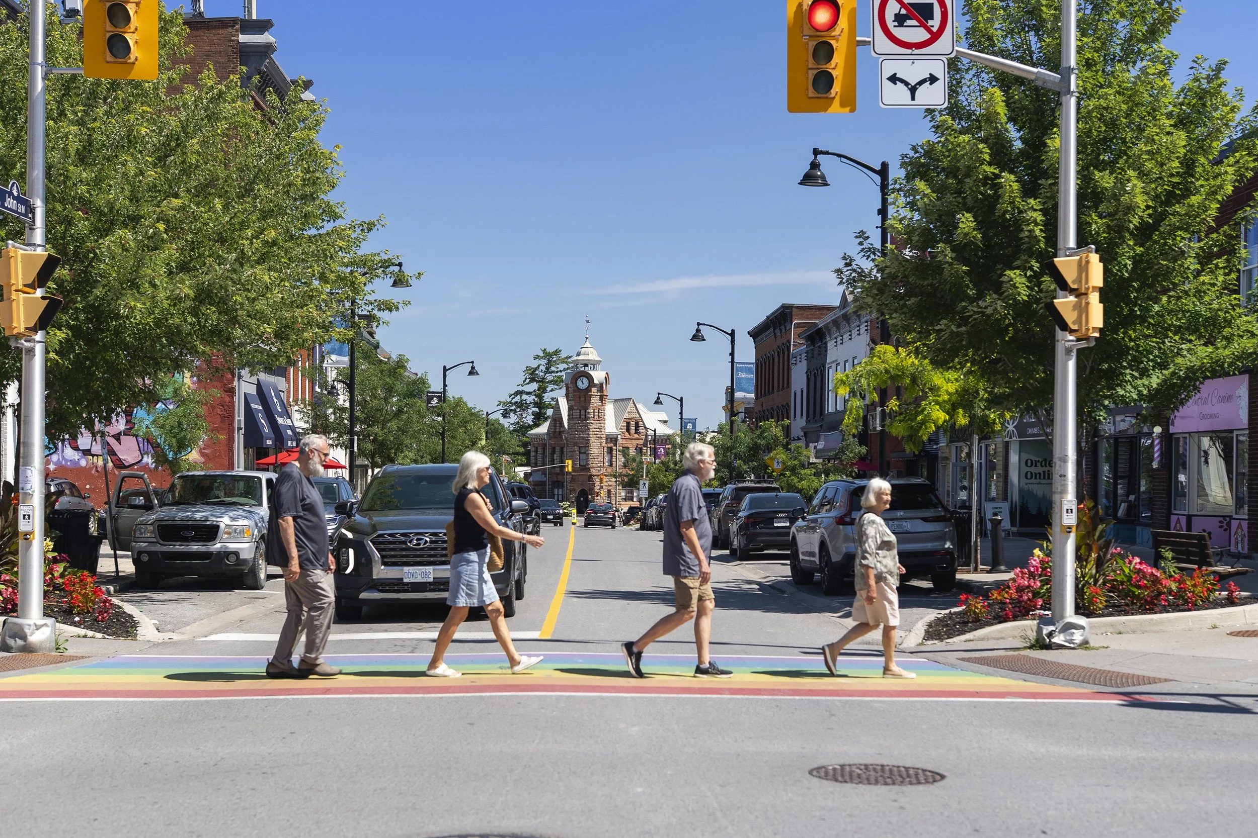 Four older adults crossing a street at a colourful rainbow crosswalk, with a historic clock tower centered in the distance
