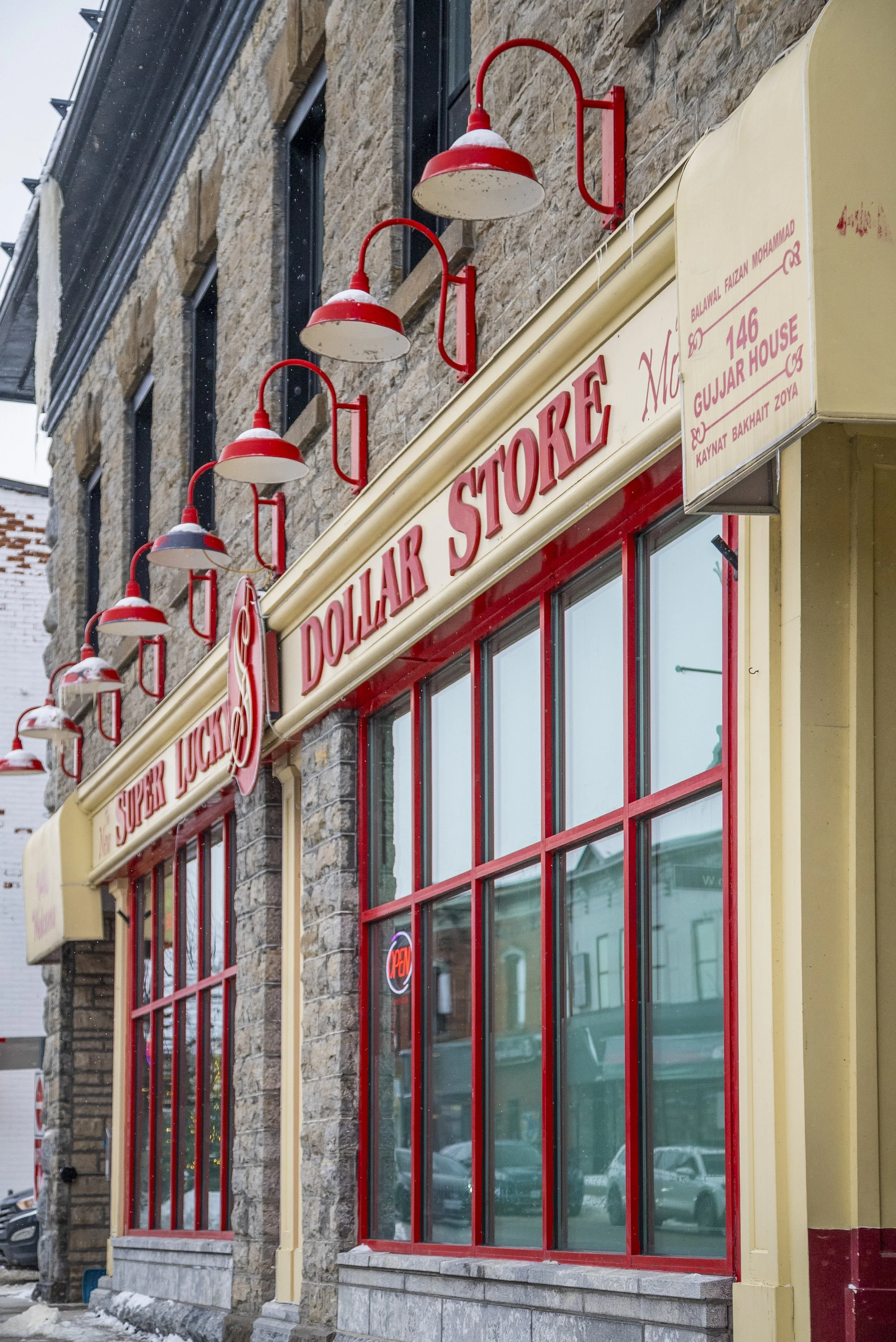 View of a storefront with large glass windows, red and yellow signage, red lamps, and a stone building facade. The sign reads 'Dollar Store' and 'Super Lucky'.