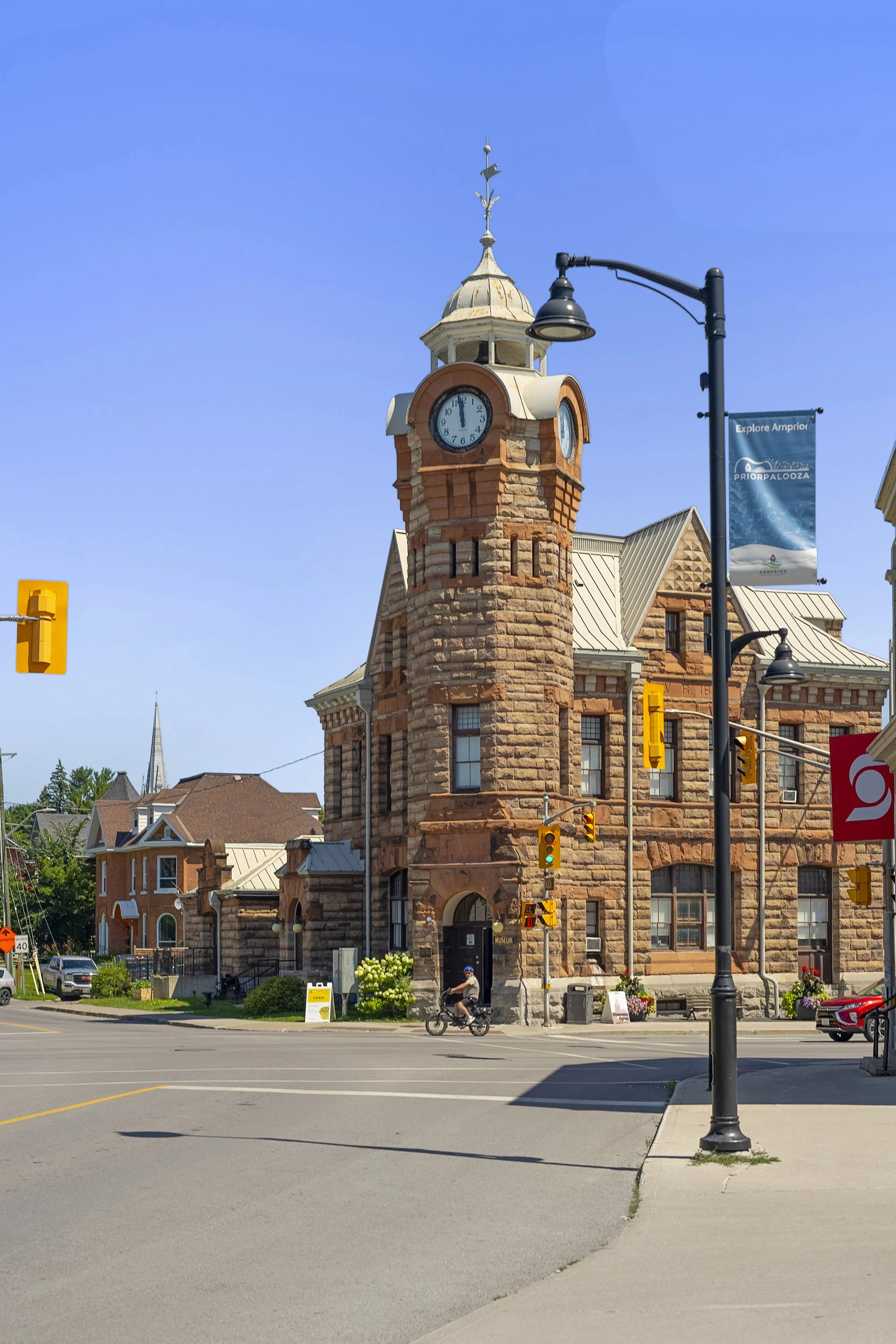 The historic clock tower building and home of the Arnprior and District Museum standing at a street intersection in Downtown Arnprior under a clear blue sky