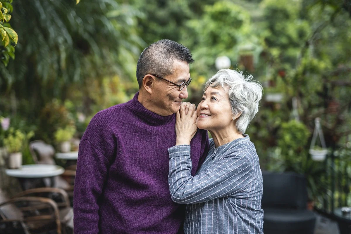 An older asian couple hugging and staring into each other's eyes, smiling.