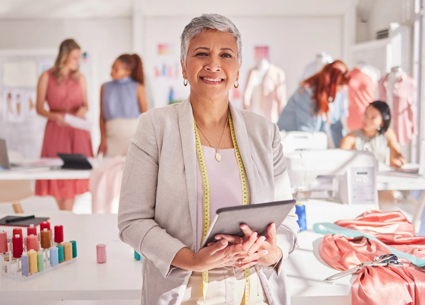 A gray-haired hispanic woman stands in her fashion business with employees talking behind her