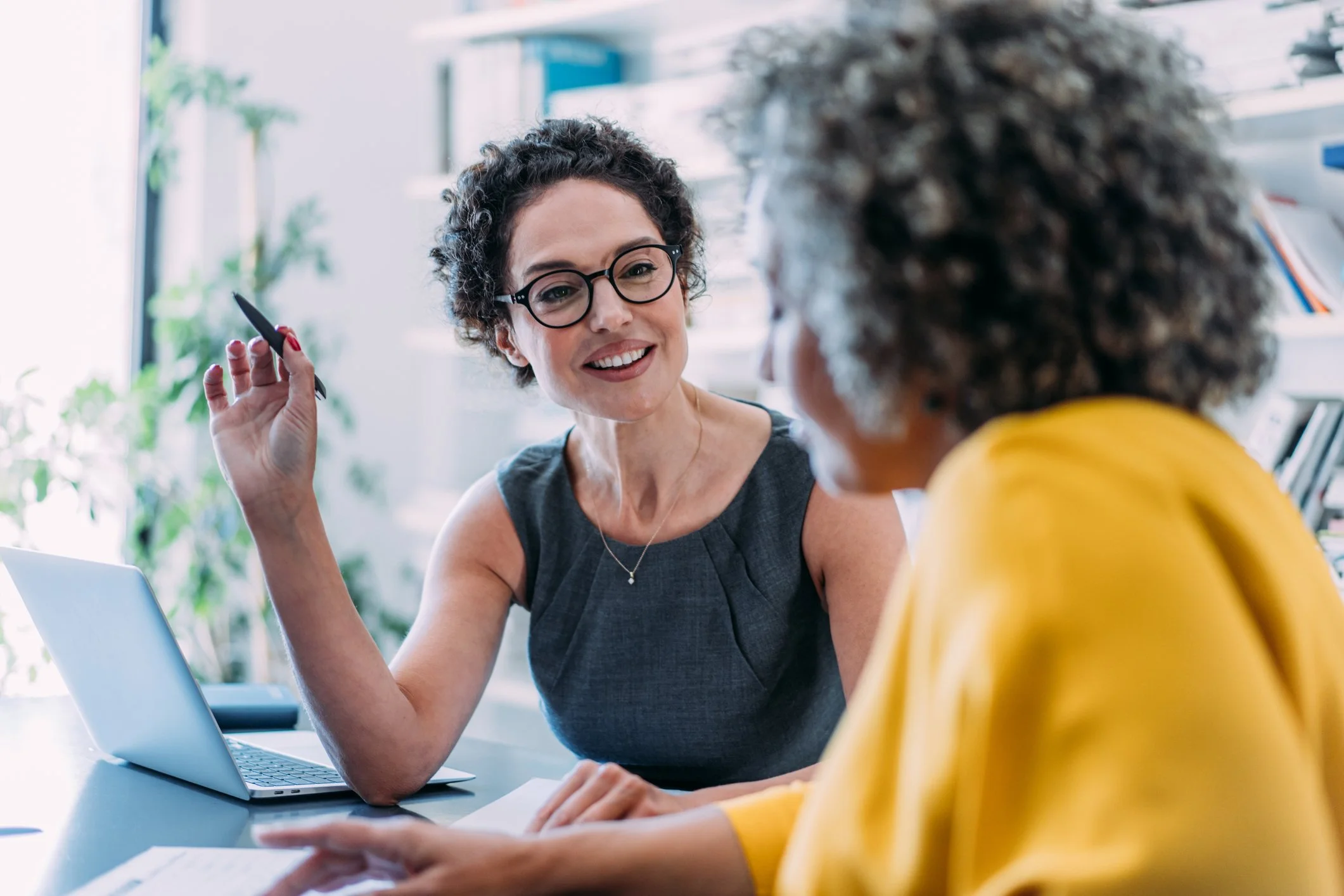 Middle-aged white female financial planner in a gray dress speaking with an older female client