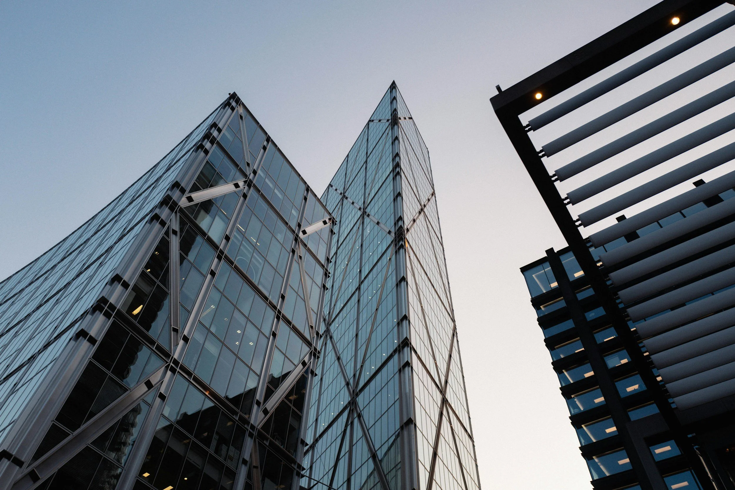 Upward view of modern glass skyscrapers with structural supports, reflecting the sky.