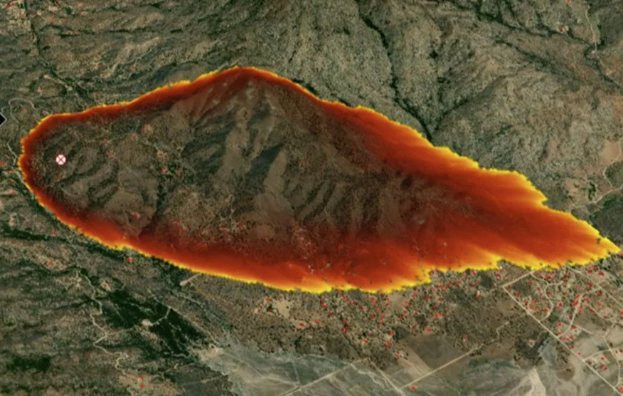 Satellite image showing a large wildfire burning in a mountainous area with smoke and flames visible along the fire perimeter.