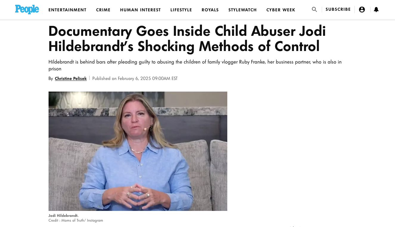 A woman with blonde hair, wearing a light blue shirt, sitting on a gray couch with her hands clasped, speaking during a video or interview.