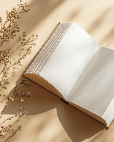 An open blank notebook with white pages, lying on a beige surface next to dried flowers with small buds.