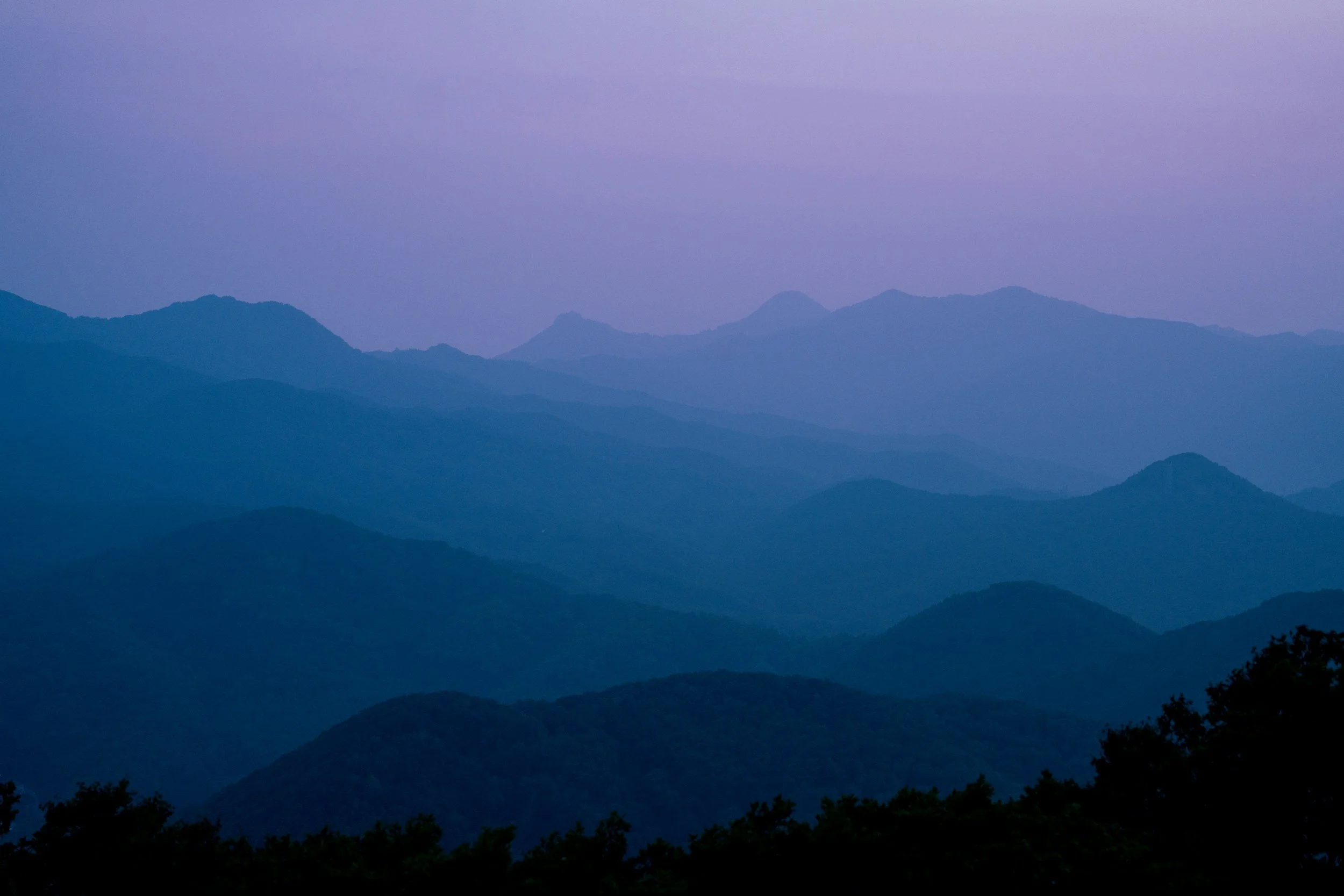 Mountain range at dusk with layered silhouettes and a purple sky.