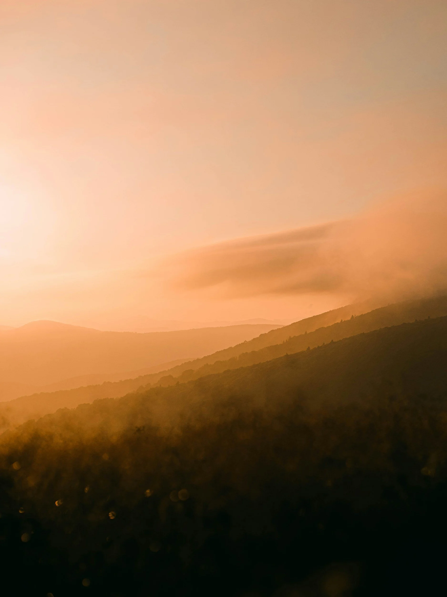 Sunset over mountains with a warm orange sky and dark silhouetted hills.