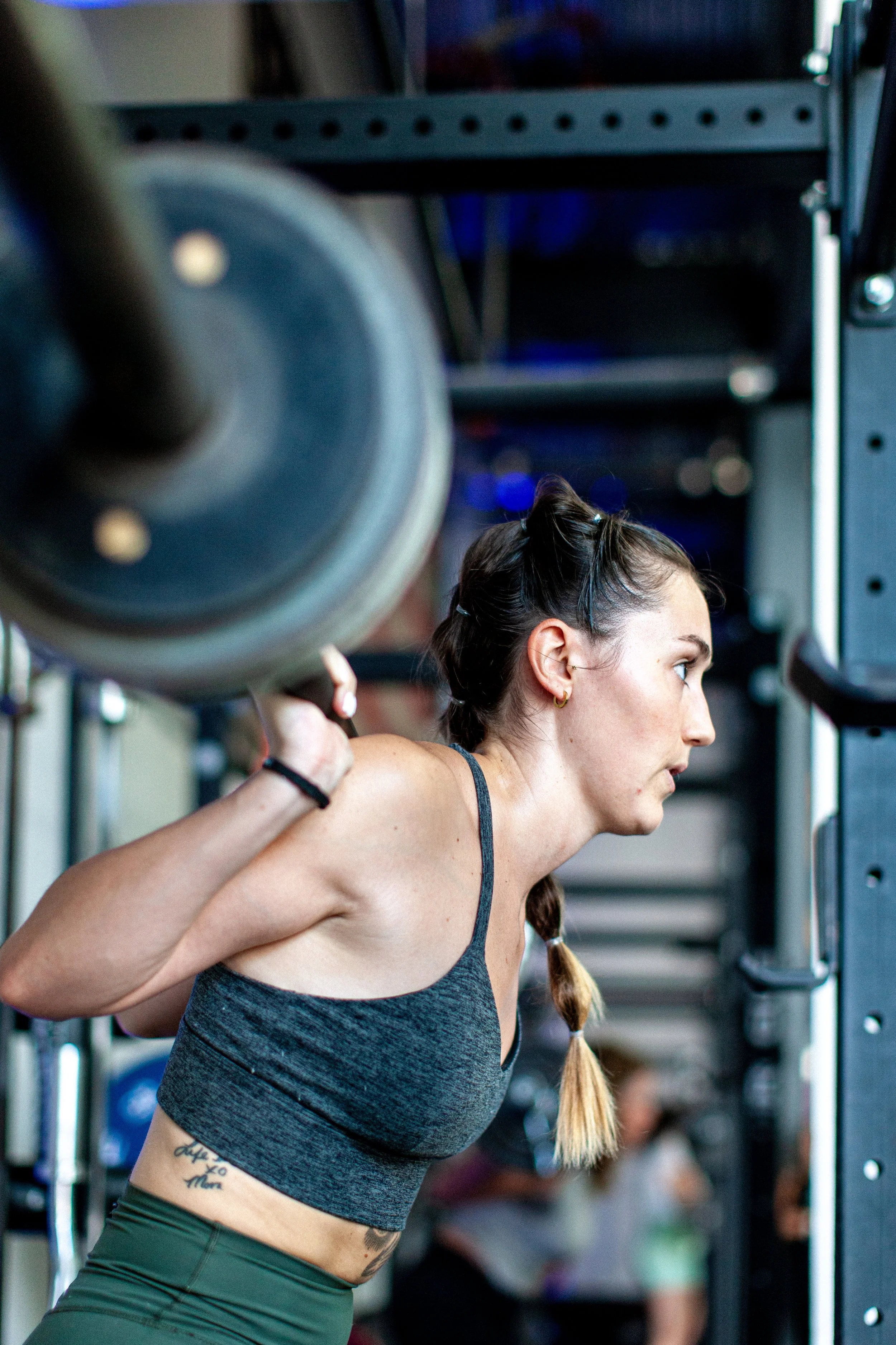 A woman with a braid performing a squat exercise with a barbell on her shoulders in a gym.
