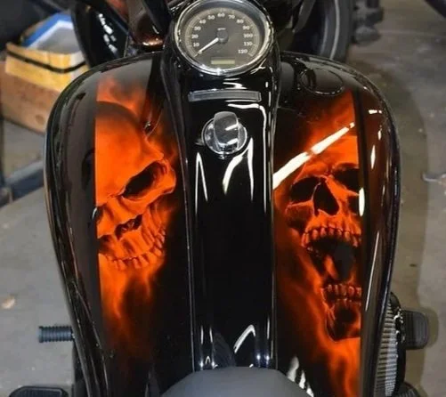 Close-up of a motorcycle fuel tank with flames and skull designs painted on it.