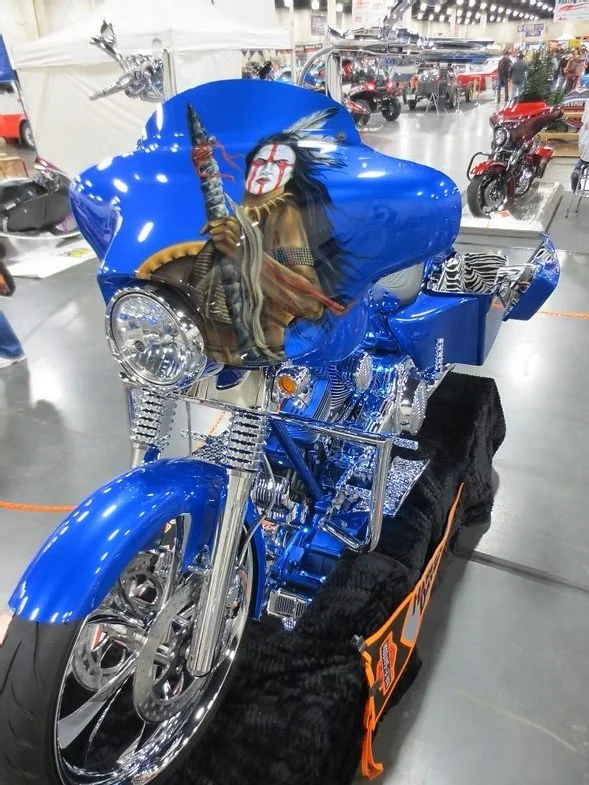 Blue custom motorcycle with eagle-themed artwork on the front fairing, displayed at an indoor motorcycle show.