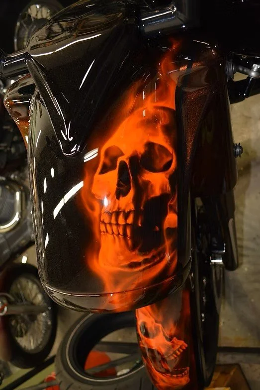A motorcycle fuel tank with a painted skull design and flames in red and orange hues.