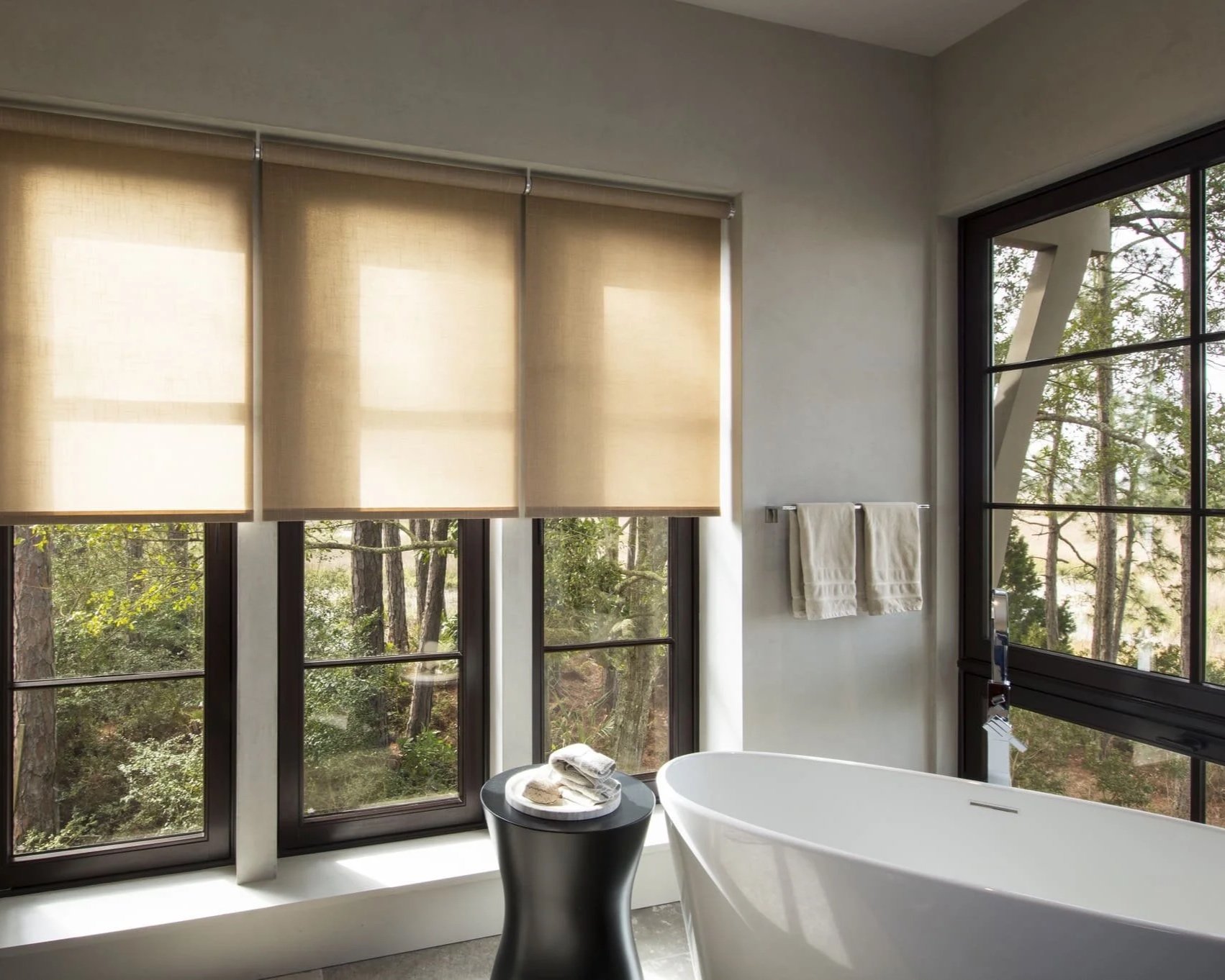 Modern bathroom with freestanding bathtub and motorized window treatments providing privacy and natural light control