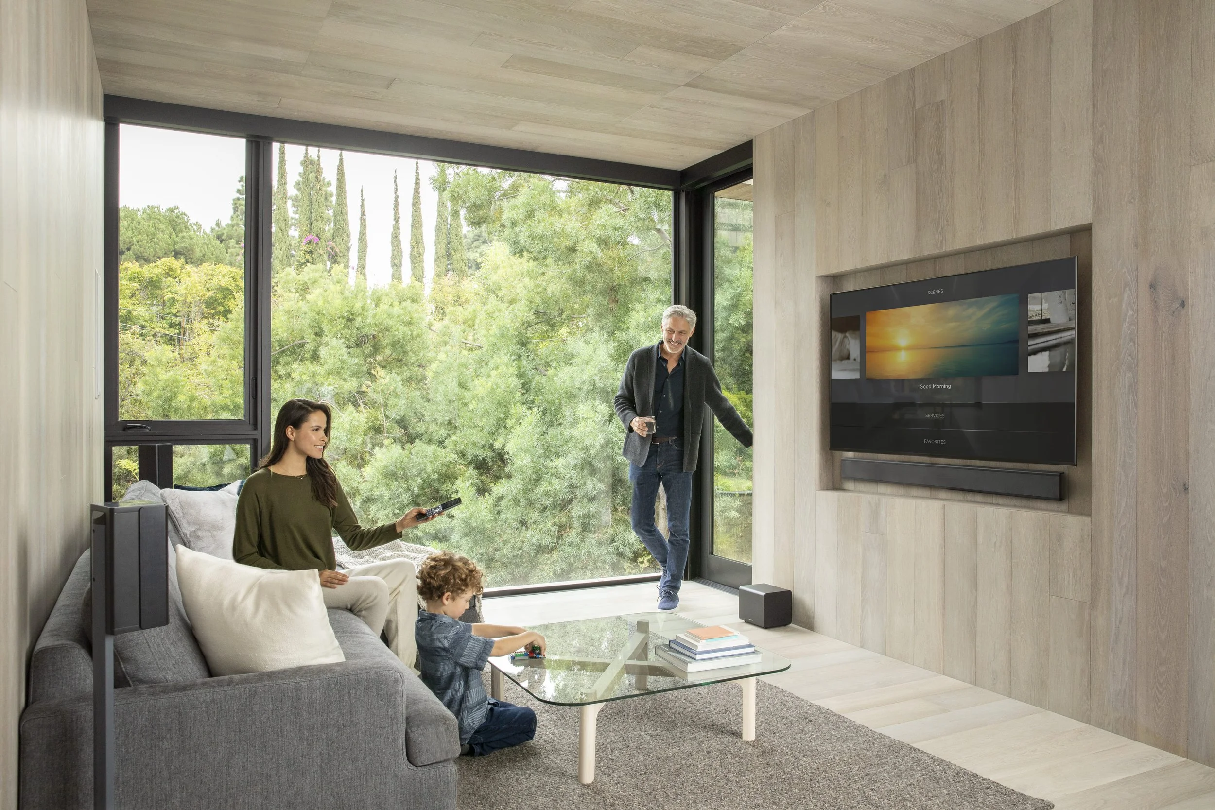 Family in a modern living room with a flat-screen TV and large windows, enjoying connected home technology
