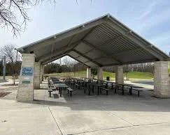 Public park shelter with picnic tables under a metal roof, supported by brick columns.