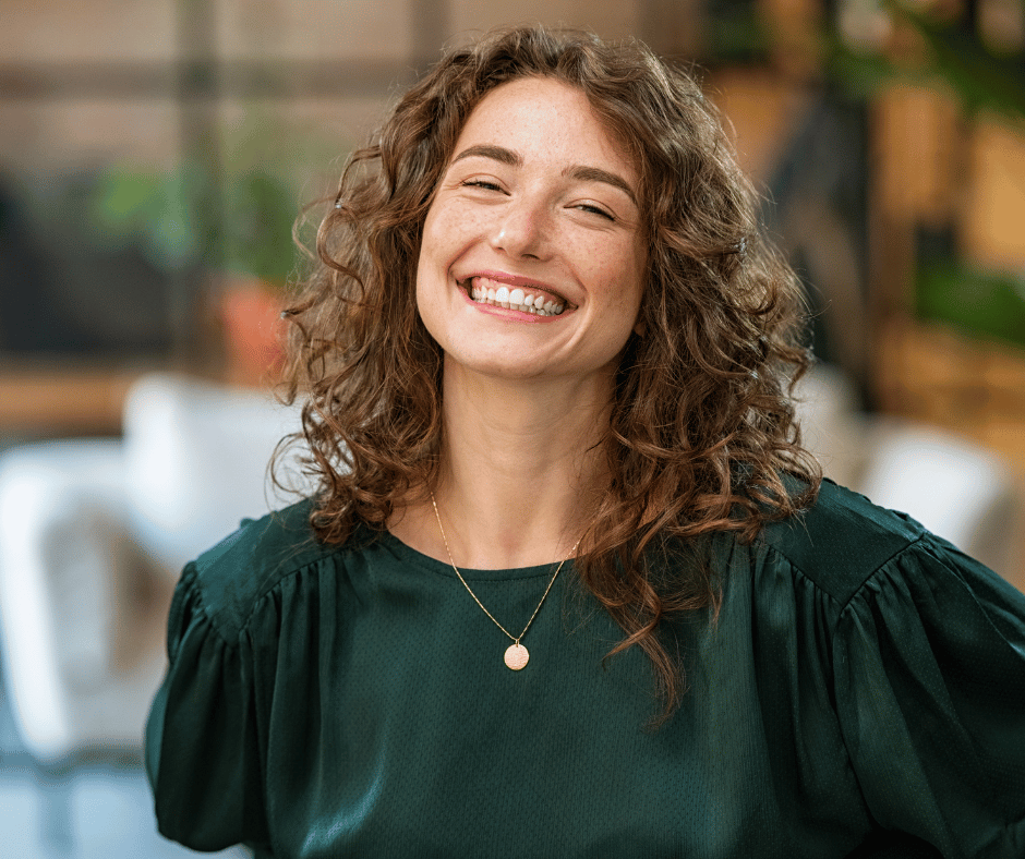 A woman with curly brown hair smiling in an indoor setting.