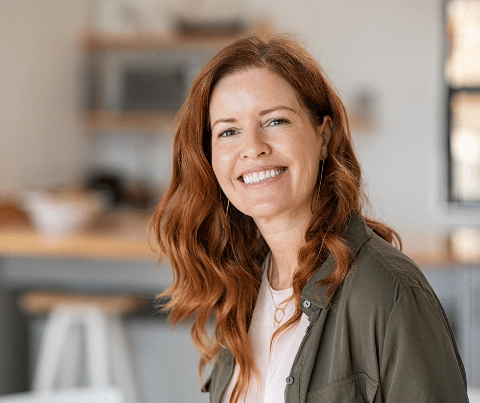 A woman with long, wavy red hair smiling in a kitchen.