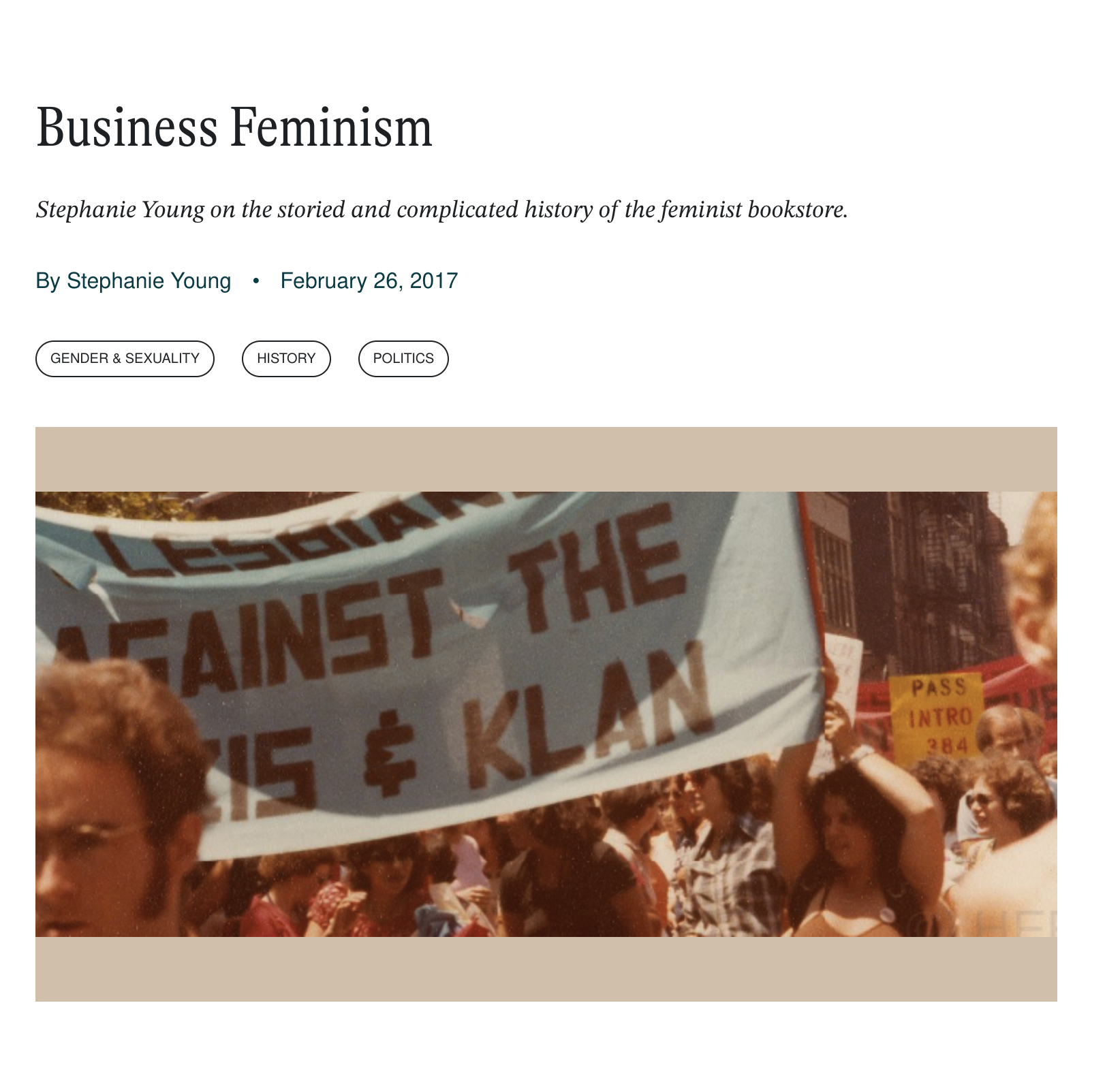 A crowd of protesters holding signs and a large banner at a demonstration against the Nazis and the Ku Klux Klan, with buildings in the background.