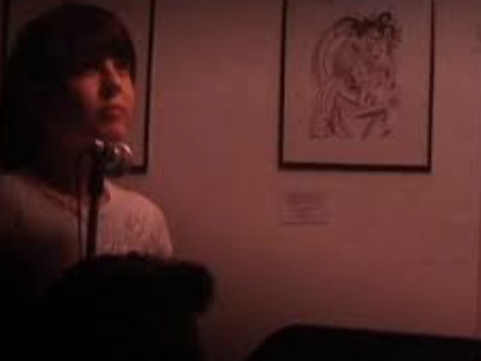 Stephanie Young standing in front of framed artwork on a wall in a dimly lit room. The room is Artists Television Access in San Francisco sometime in the 2000s.