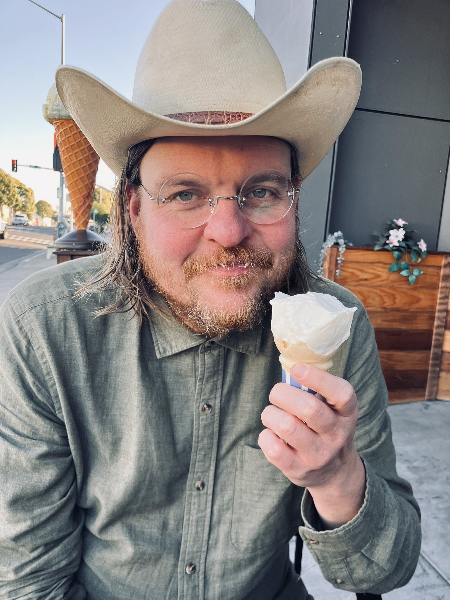 A photograph of poet Brandon Brown wearing a cowboy hat, chambray shirt, and holding an ice cream cone. 