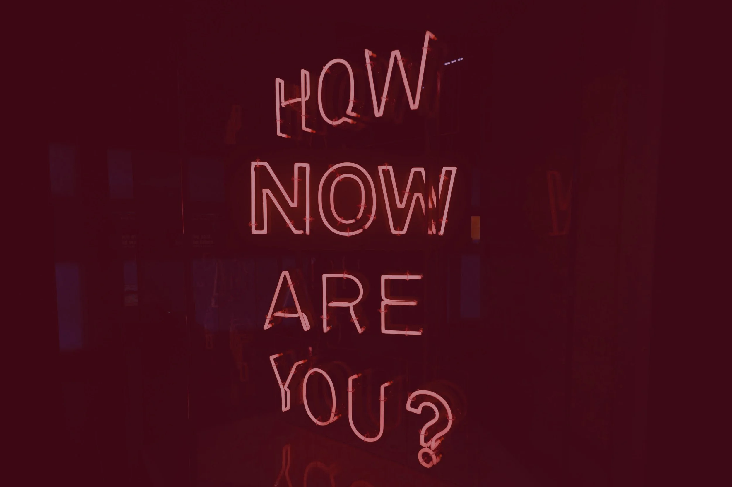 Pink neon sign that reads "NOW" in the top line and "ARE" in the bottom line, reflected in a dark surface.