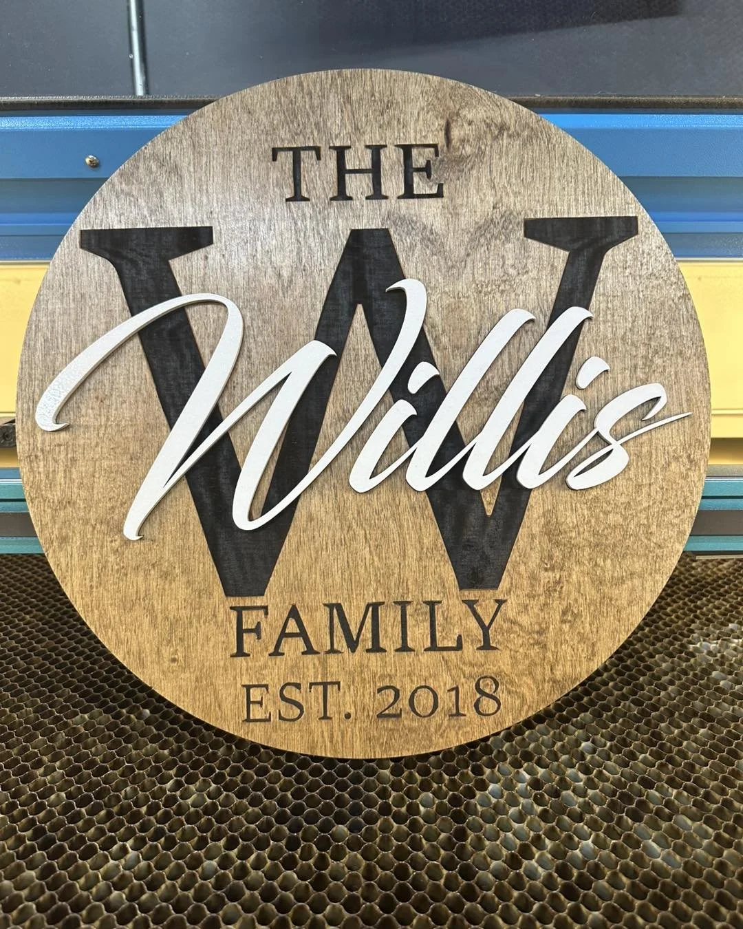 Wooden round sign with the words 'The Wilds Family' and 'Est. 2018', featuring a large black letter 'W' in the background and white cursive text 'Wilds' across it.