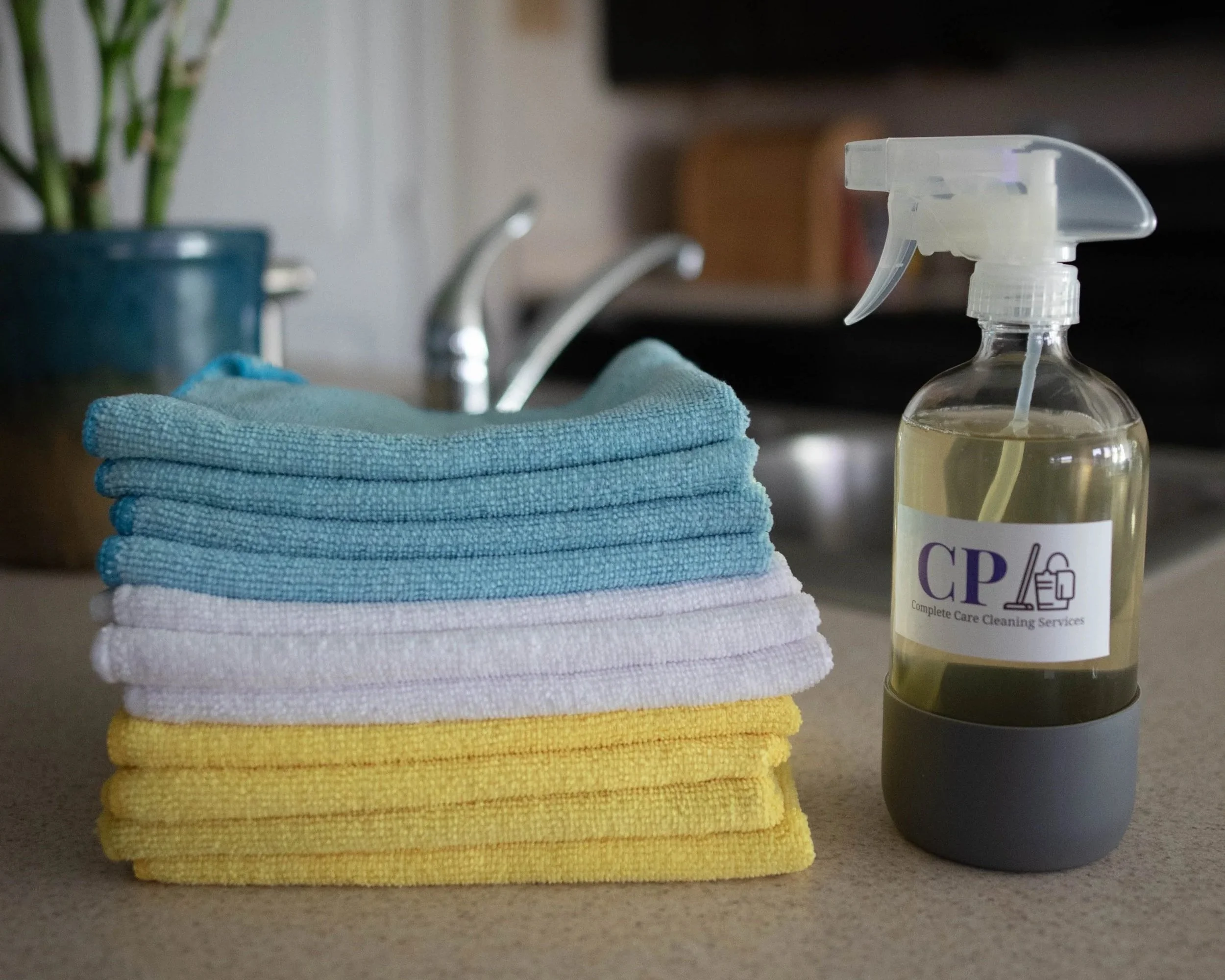 Stack of colorful cloth towels on a kitchen counter with a spray bottle of cleaning solution nearby.