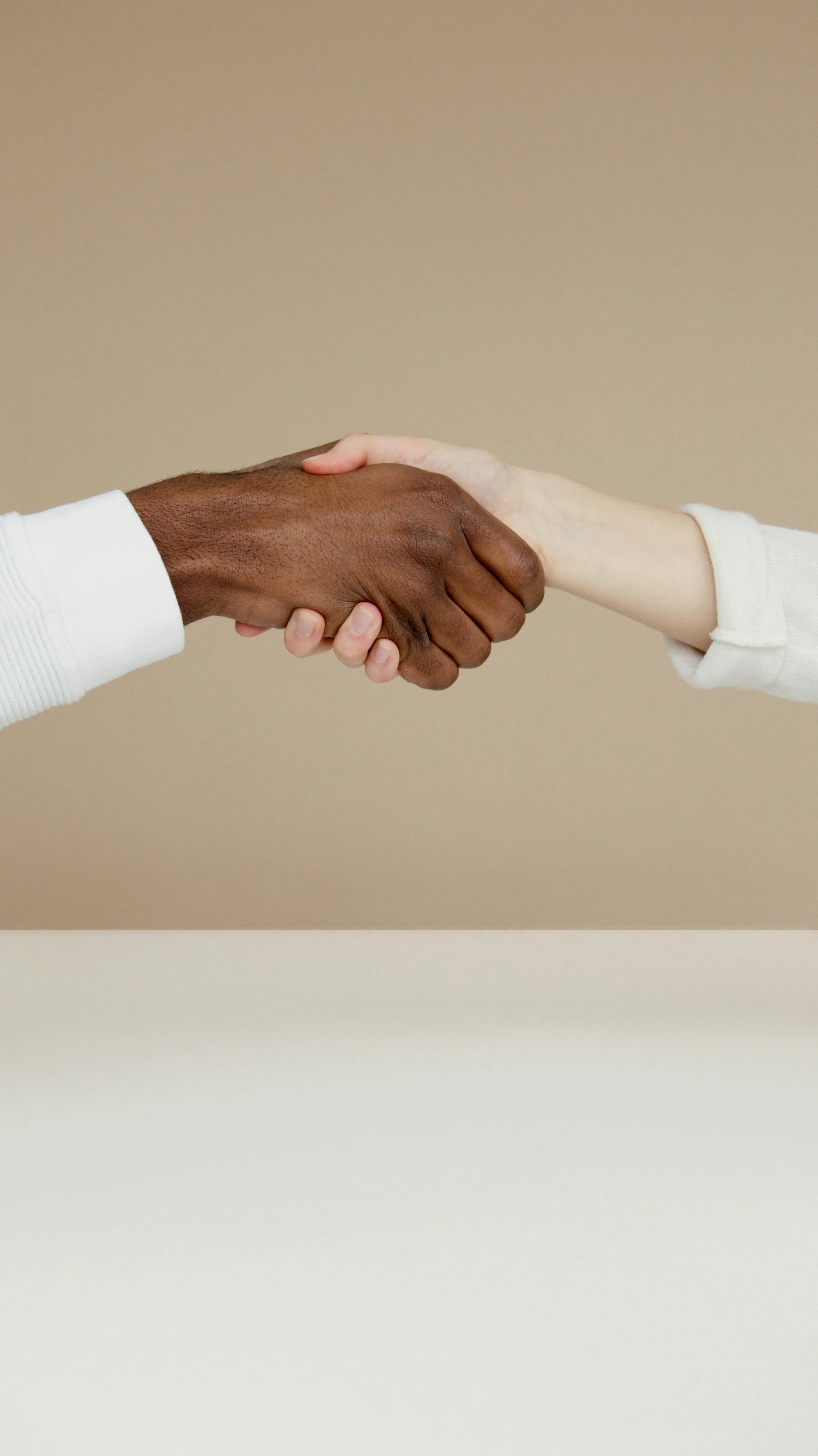 Close-up of two people shaking hands, one with dark skin and the other with light skin, against a beige background.