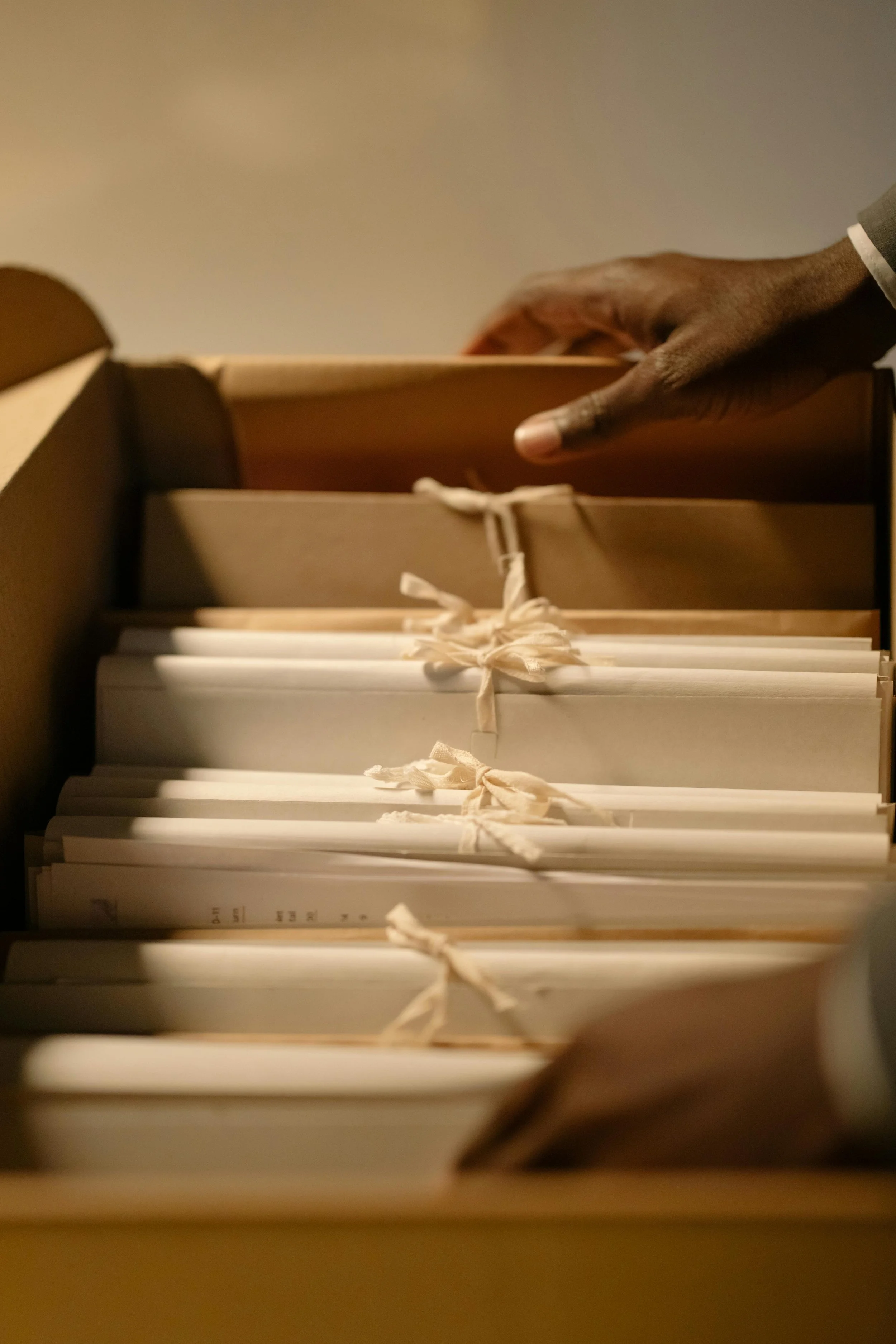 A close-up view of a person’s hand reaching into a box filled with tied paper packages or documents.