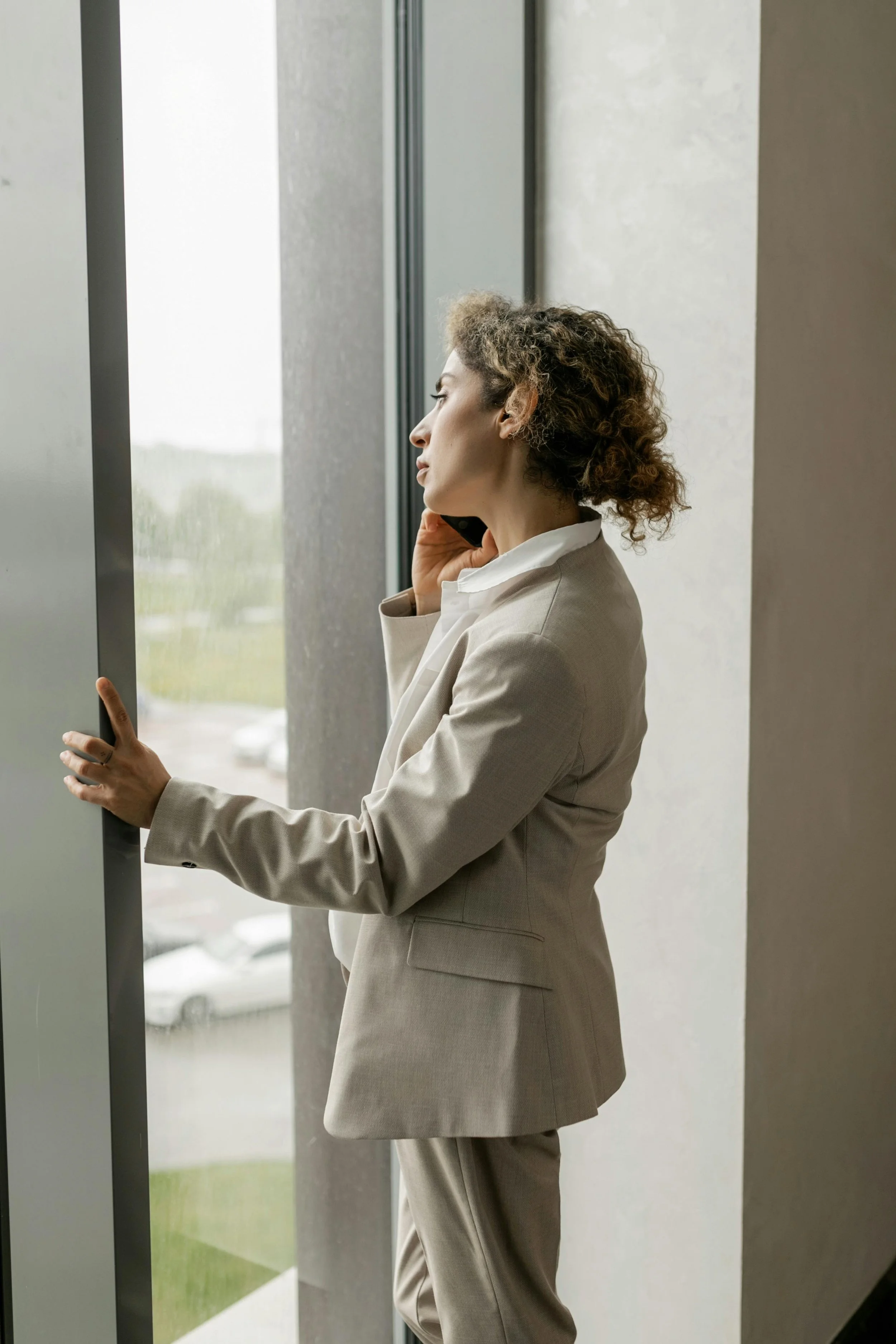 Businesswoman talking on cell phone near large window.