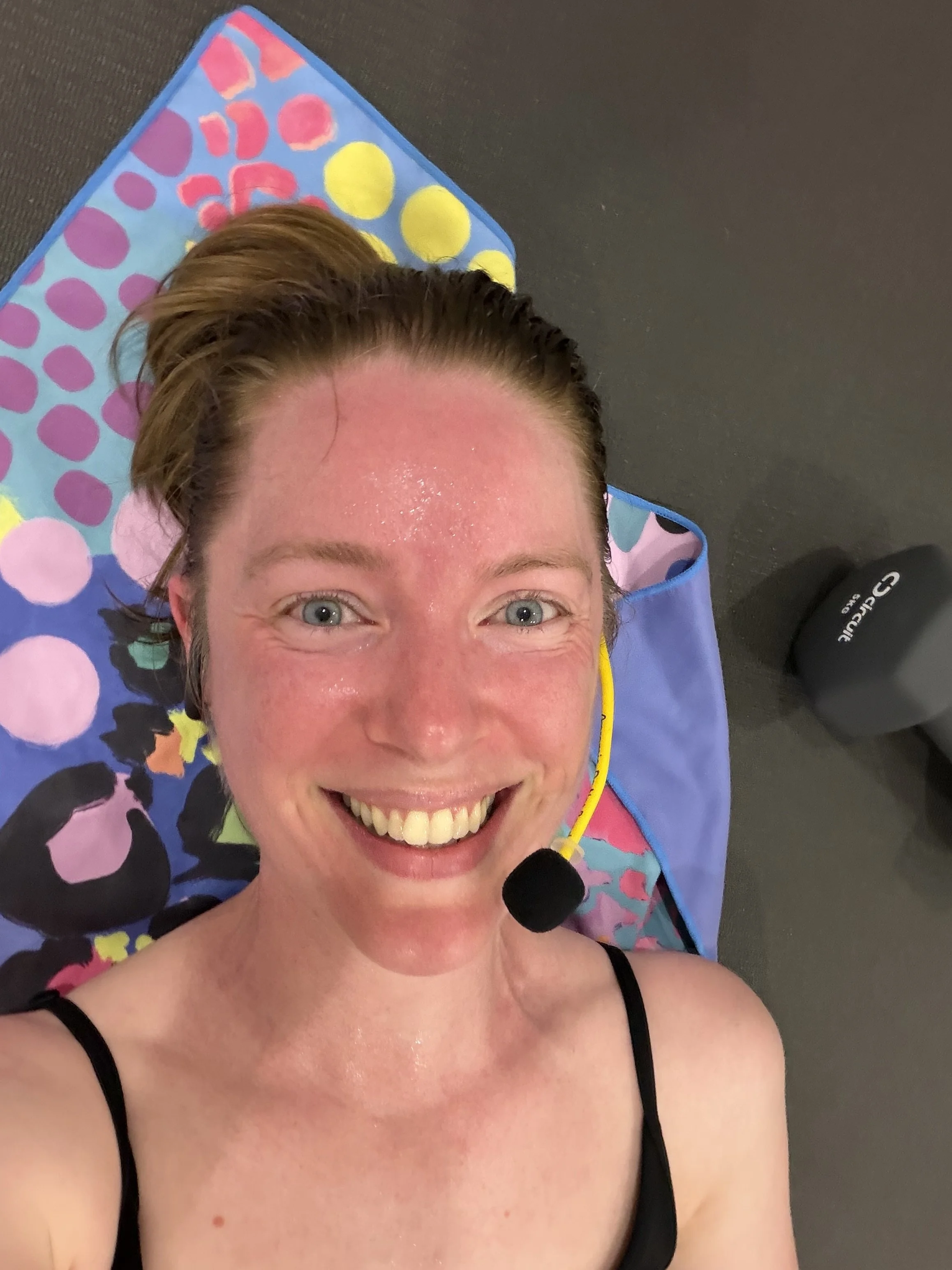 Instruvtor Fiona lying on a yoga mat, smiling and looking sweaty, wearing a microphone