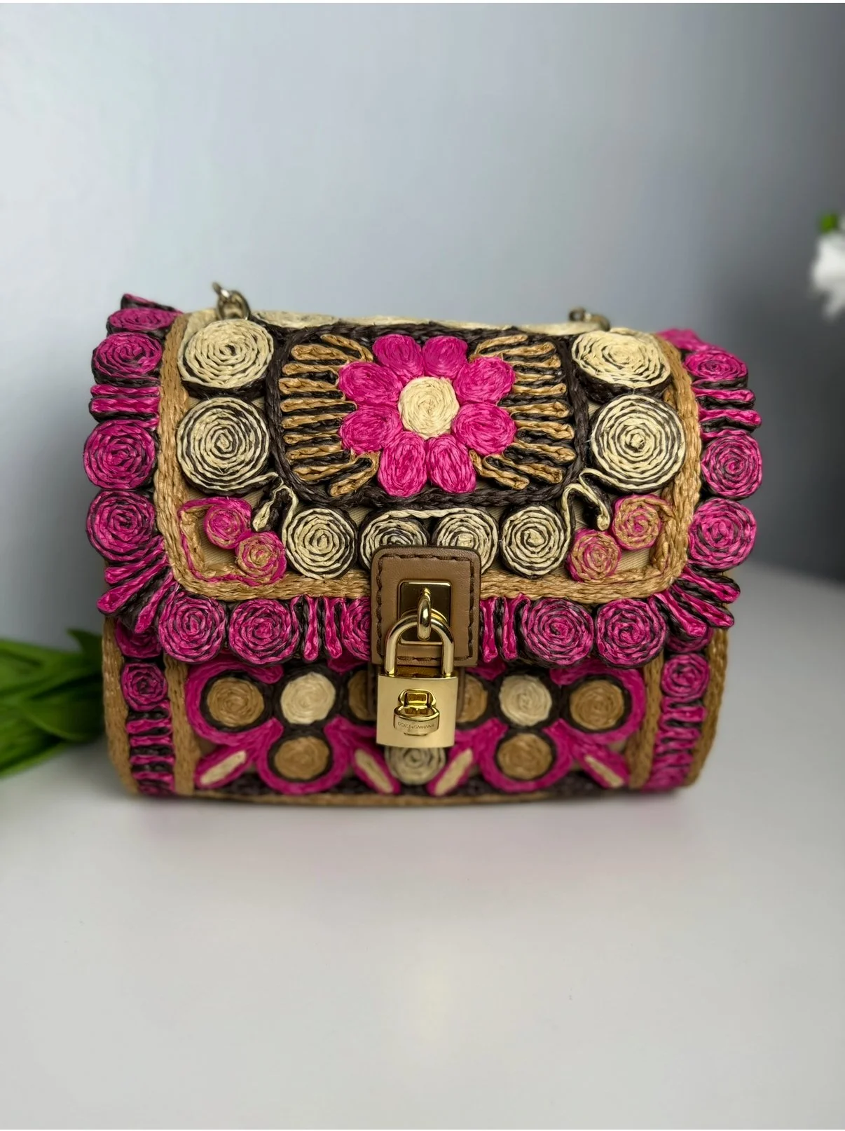 A handbag decorated with spiraled woven designs in pink, cream, and black, featuring a gold lock clasp on the front.