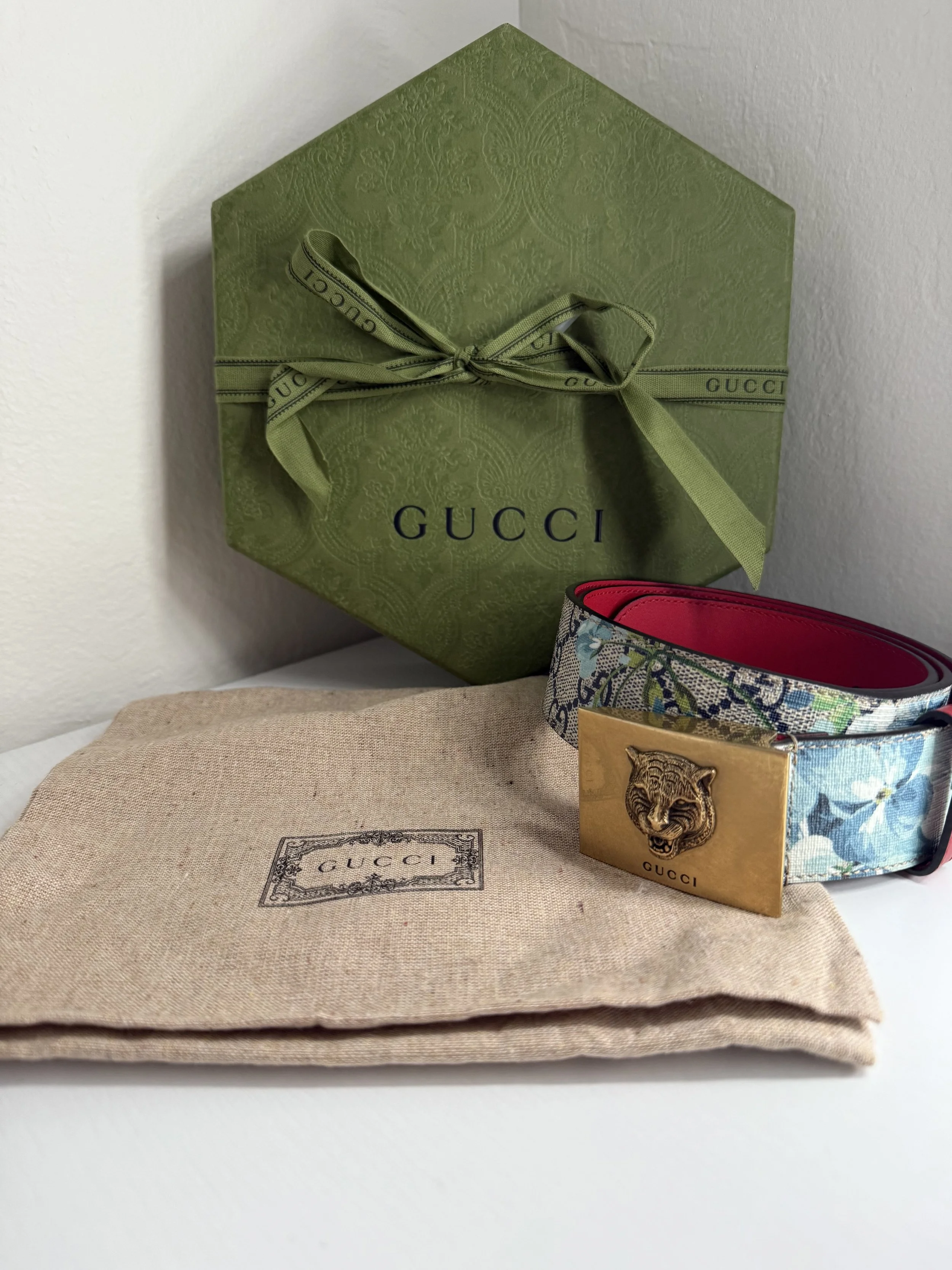 Gucci box, belt with tiger head buckle, and dust bag on a white surface.
