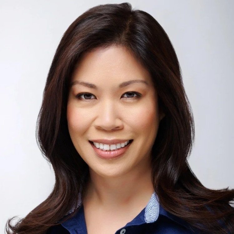 Headshot of a smiling woman with dark brown hair wearing a blue top against a white background.