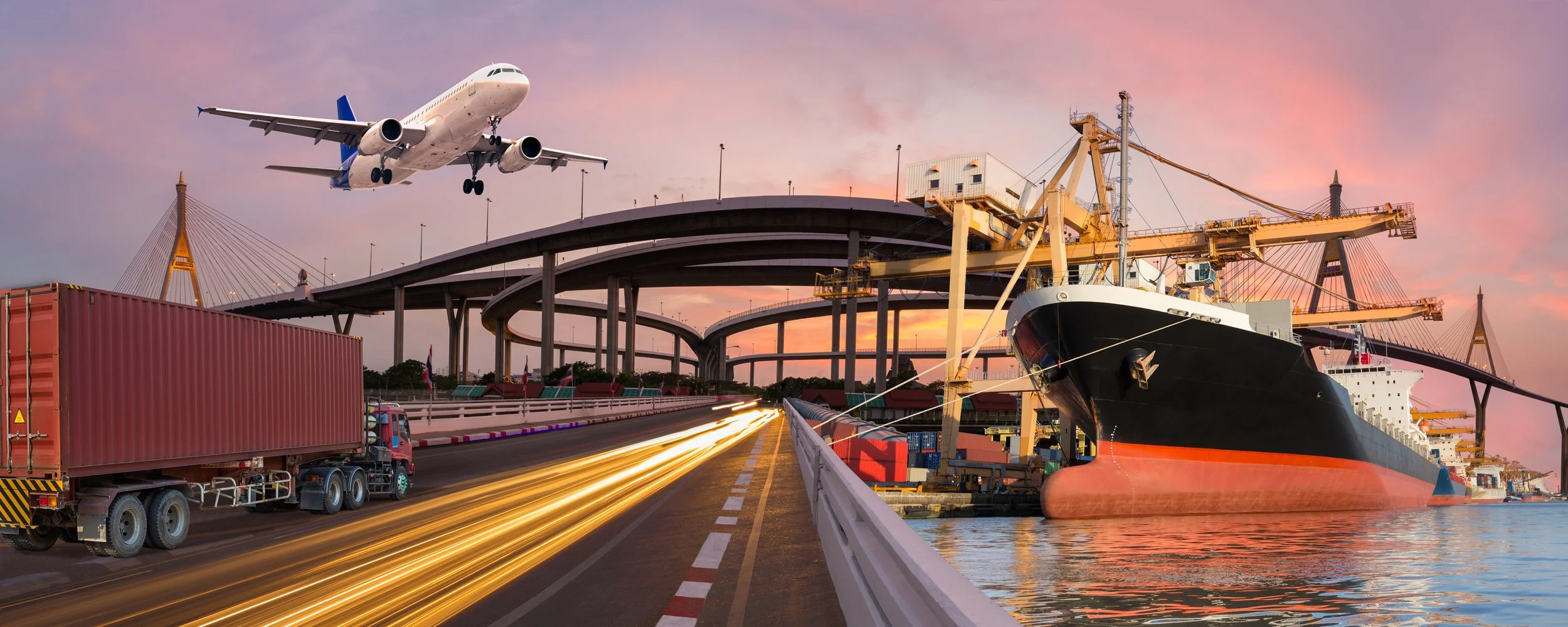 An airplane flying above a busy port with a cargo ship docked, a highway with streaks of light from moving vehicles, and a bridge at sunset.