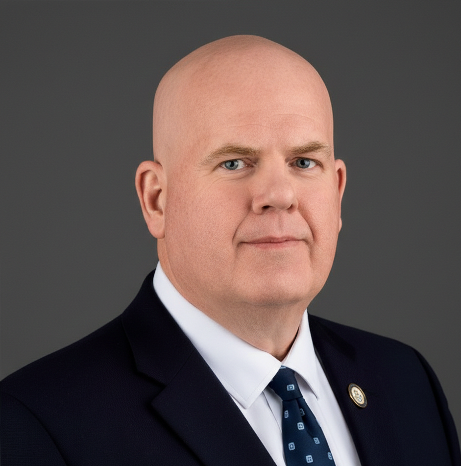 A bald man wearing a suit and tie posing for a professional portrait.