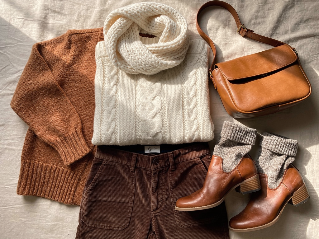 Cozy aesthetic wardrobe essentials flat lay with cable knit sweater, corduroy pants, leather boots, chunky scarf and cognac bag