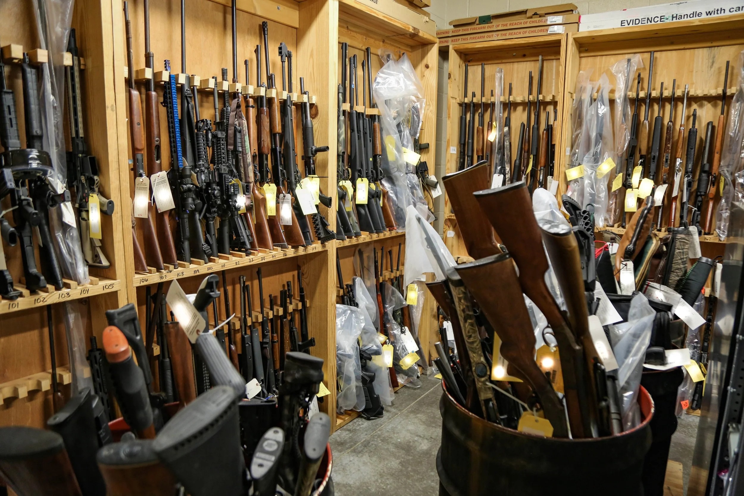 Gun store with multiple rifles and shotguns on wooden shelves and in bins.