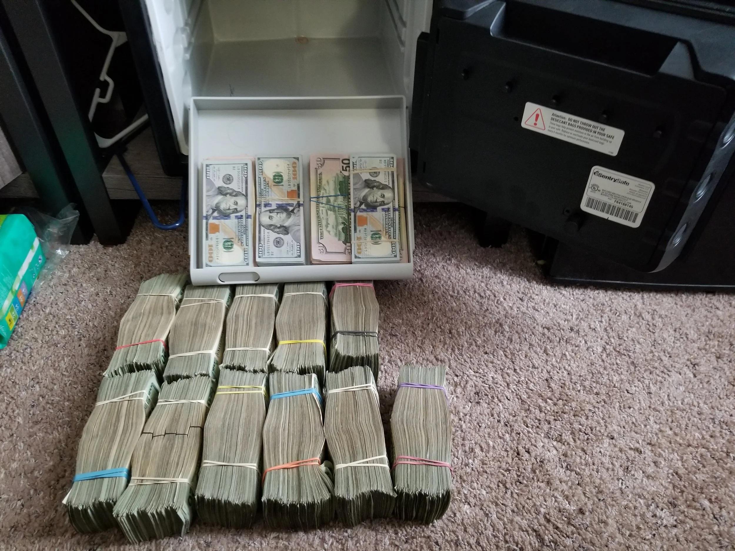 A collection of large bundles of cash, including rolls of Australian dollar notes and stacks of U.S. dollar bills, arranged on a carpeted floor next to a safe.