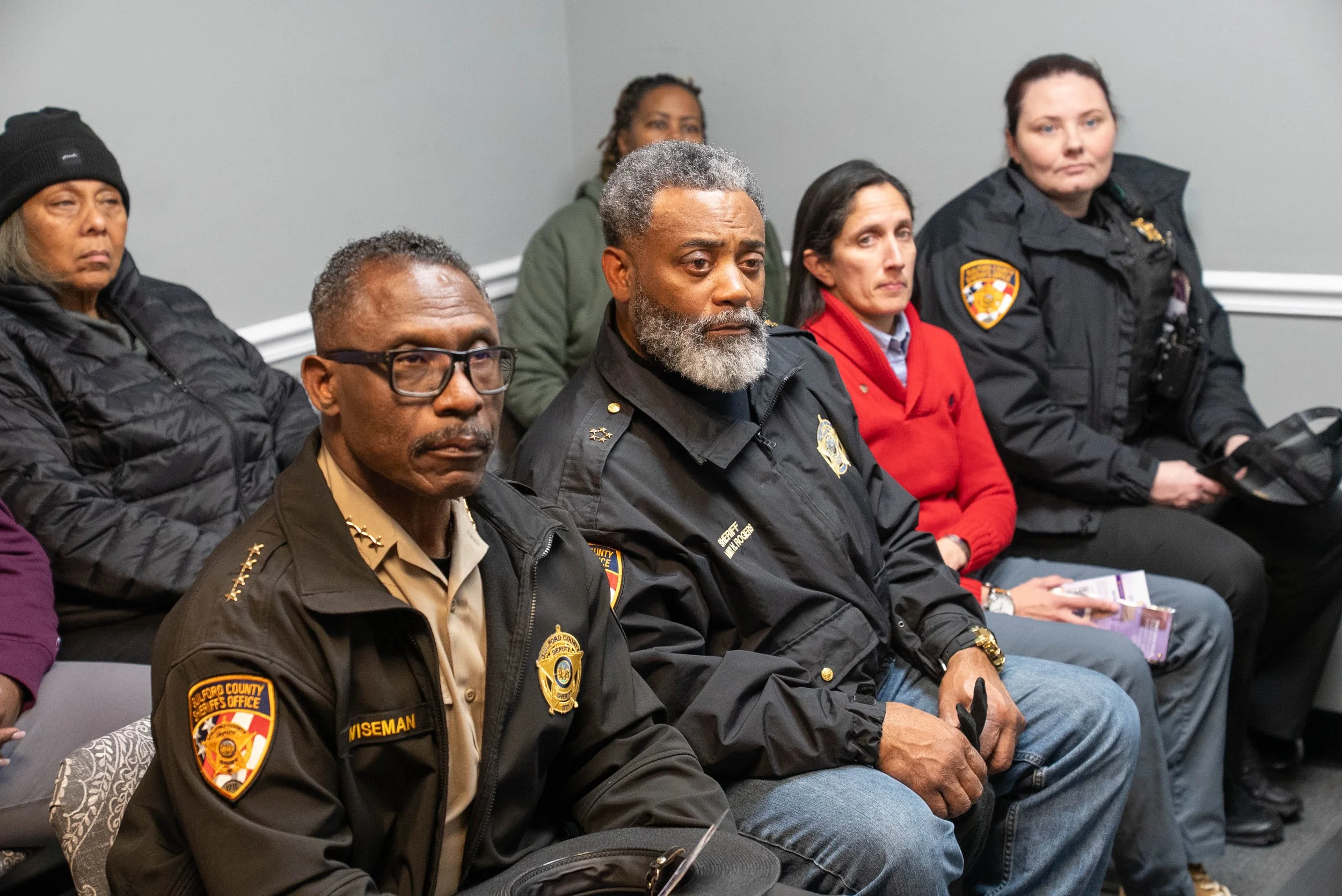 Group of people, including police officers and civilians, seated during an indoor meeting or event, listening attentively.