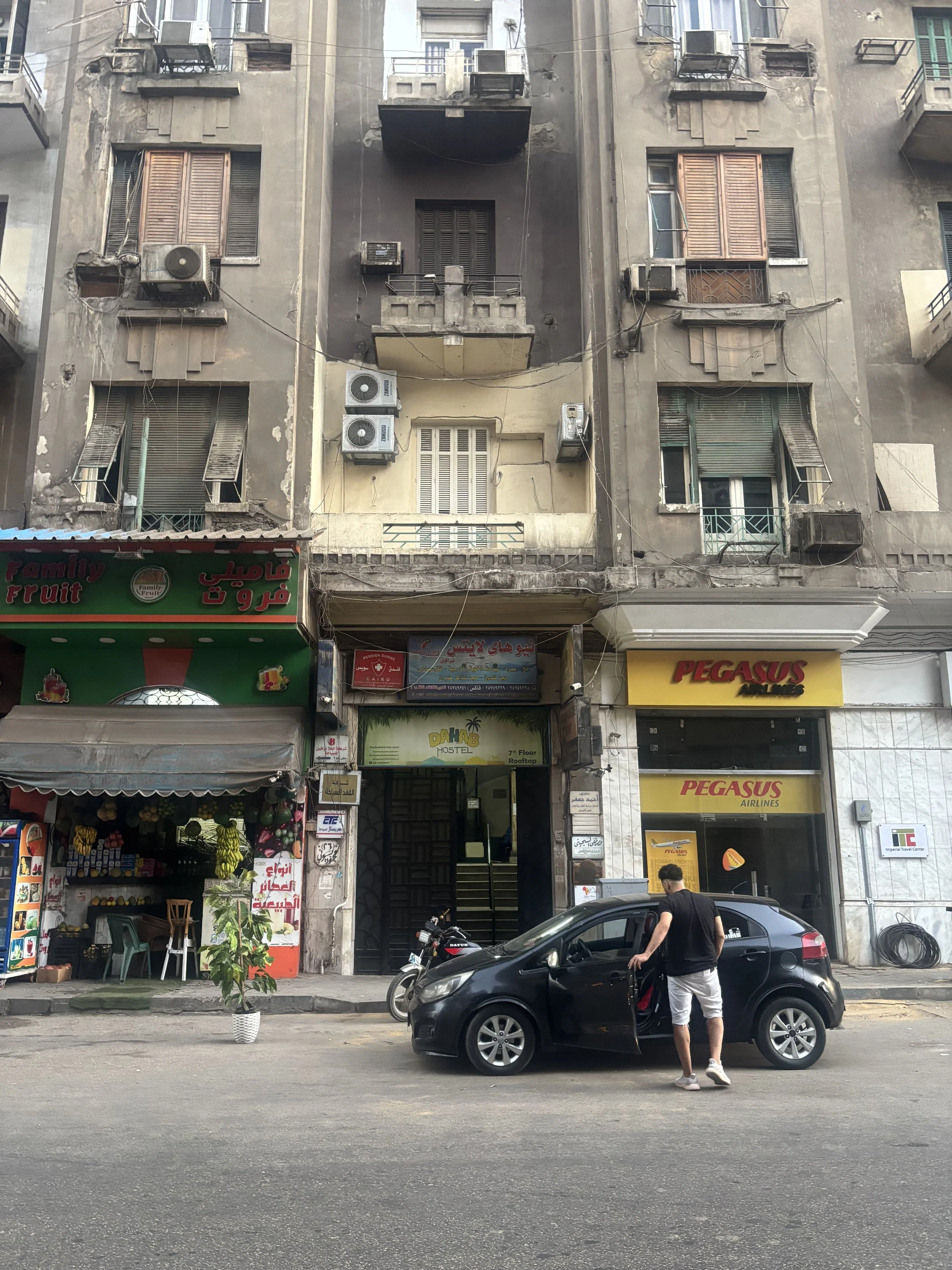 Apartment buildings in downtown Cairo with street-level shops and parked cars, showing everyday city life in Egypt.