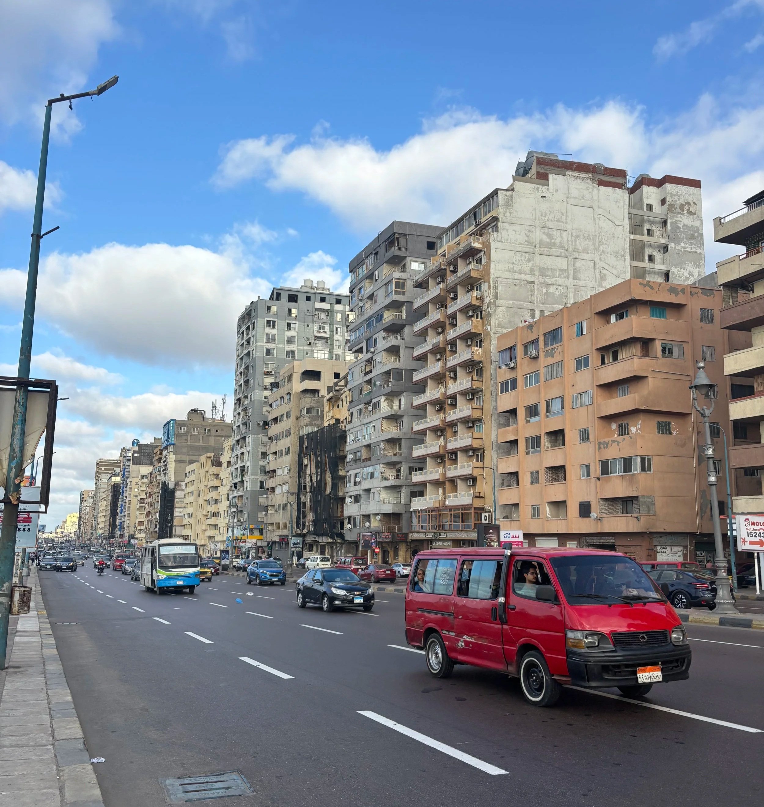 Traffic moving through a wide street in alexandria with mid-rise apartment buildings and a bright blue sky overhead.