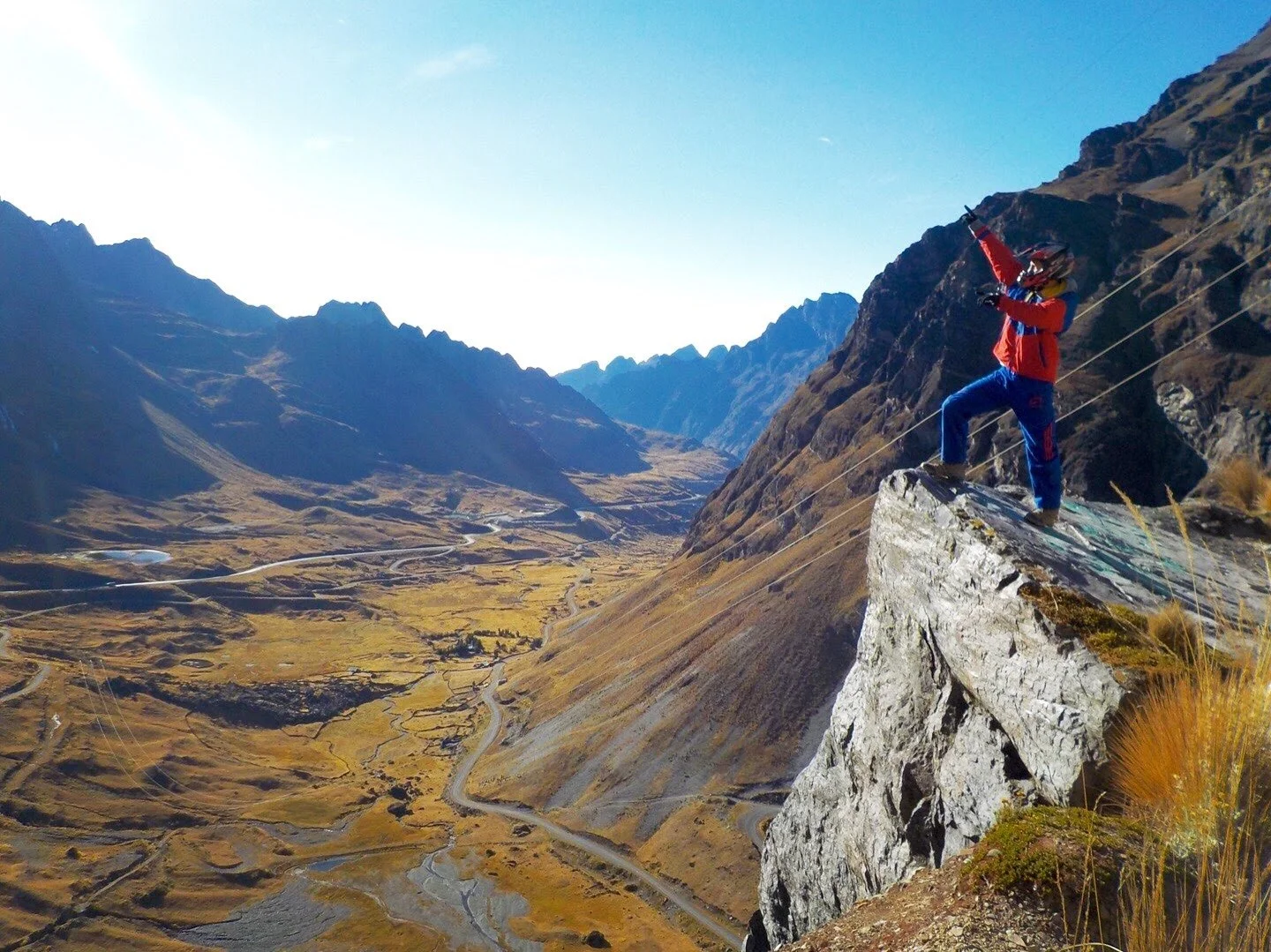 Mountain biker standing on a cliff edge overlooking the winding Death Road in Bolivia with deep valleys and Andes mountains below