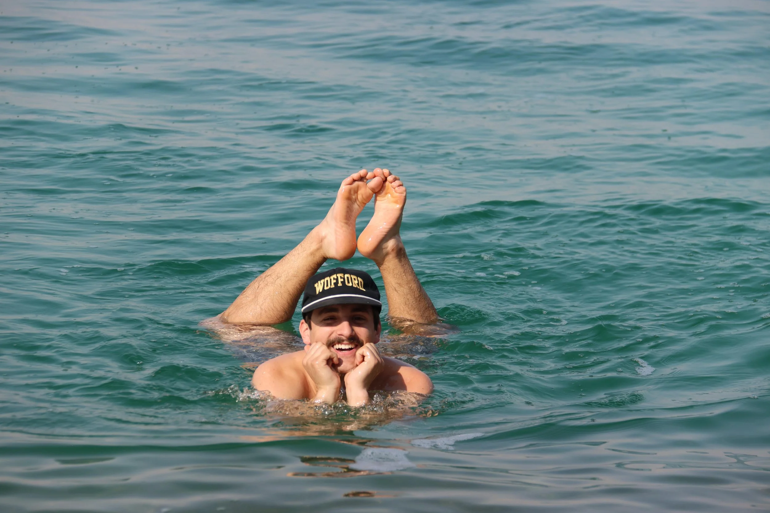 Traveler floating effortlessly in the Dead Sea near Jordan, smiling with feet raised above the water due to the extreme salt buoyancy